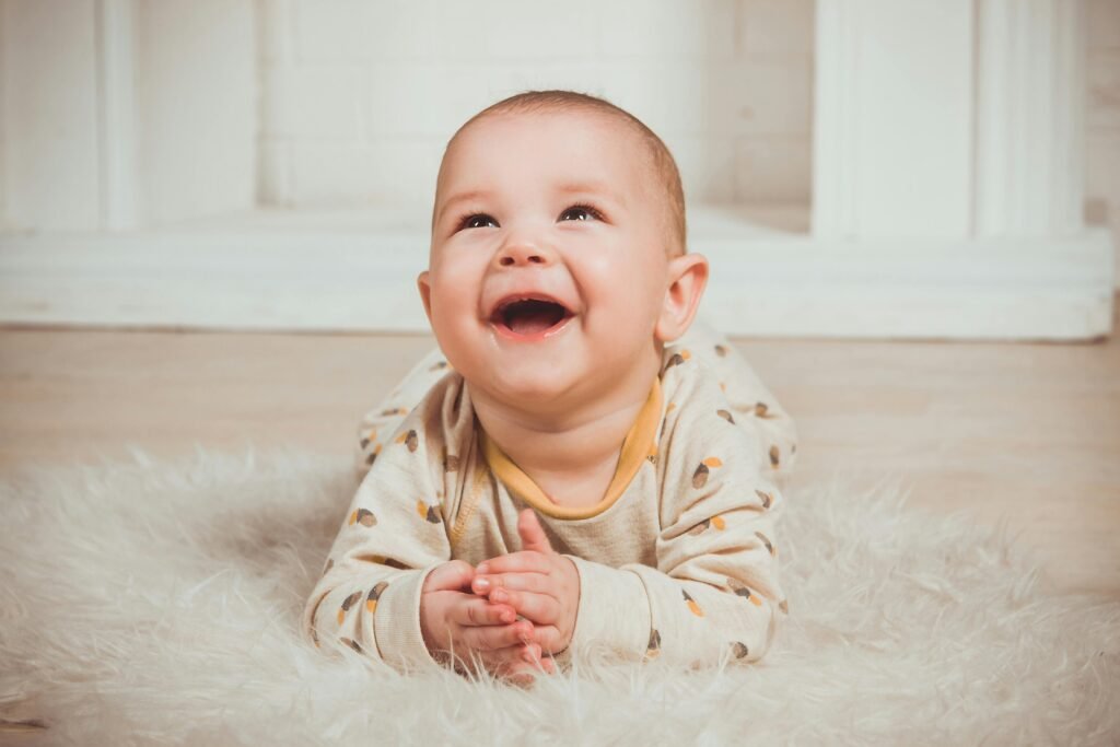 pexels-photo-1648383-1648383 Joyful baby lying on a fluffy rug, smiling and looking upwards indoors.