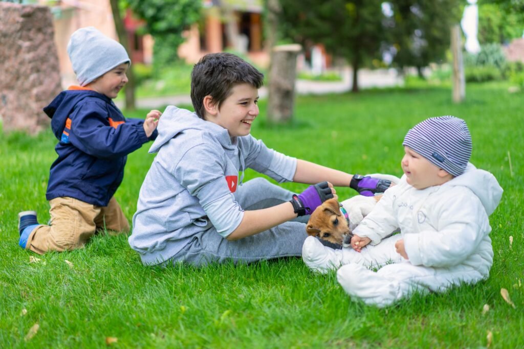 Three children enjoy a day outdoors, playing with a small puppy on a vibrant green lawn.