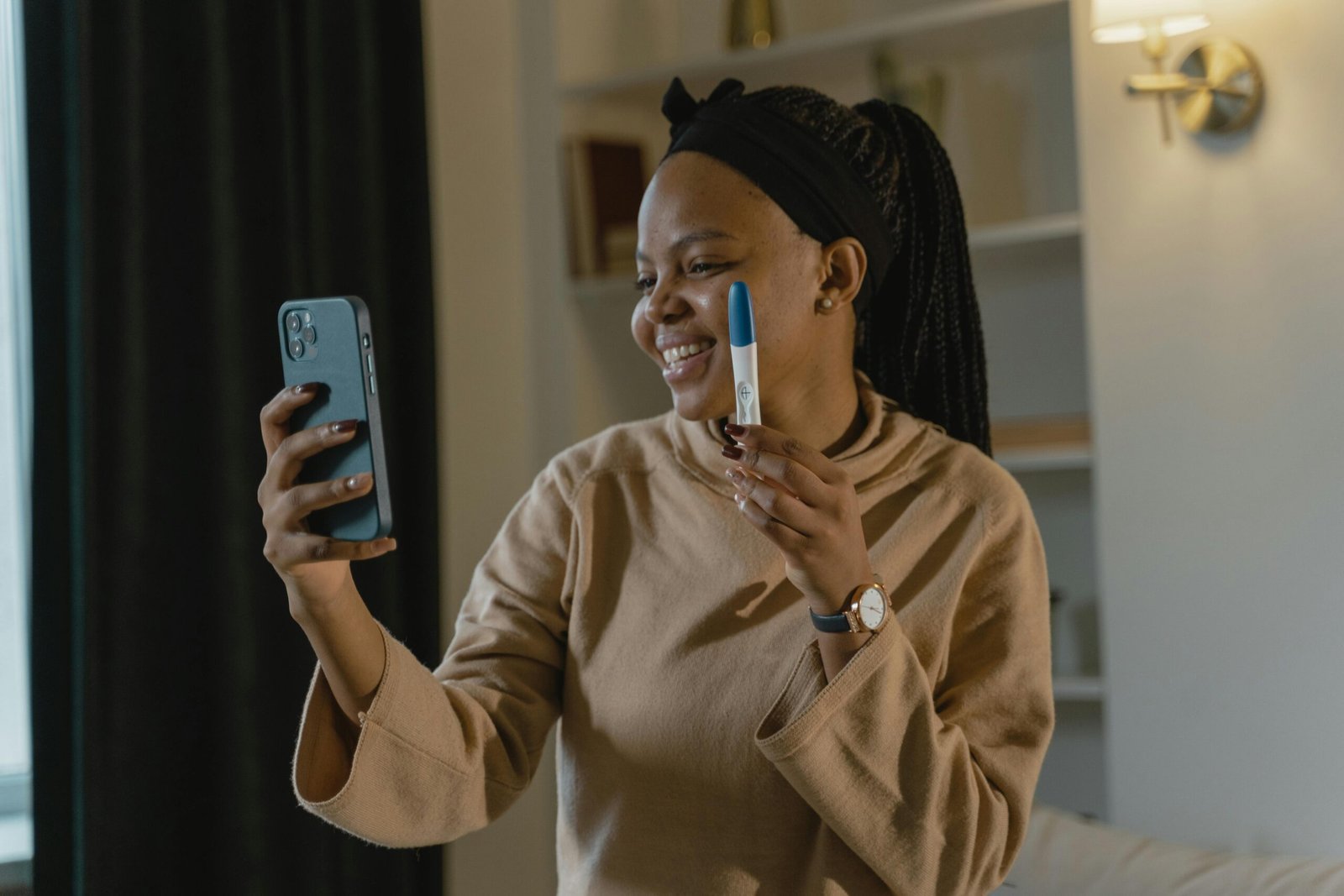 Joyful woman holding a positive pregnancy test while video calling indoors.