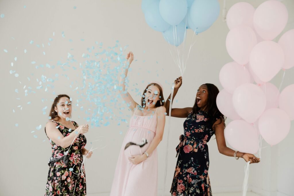 Three women celebrating a joyful gender reveal party with balloons and confetti indoors.